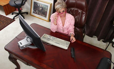 Superb american blond mature Sierra Smith in fancy skirt exposes her ass and bald pussy in office