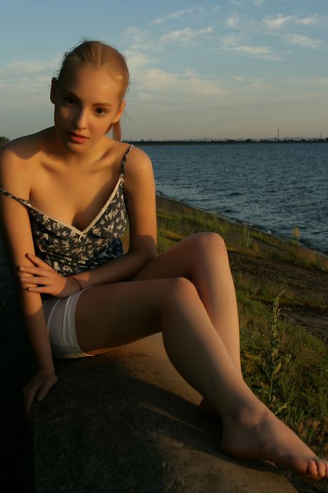 Slender teen Kira W strips naked & spreads her long legs on a bed