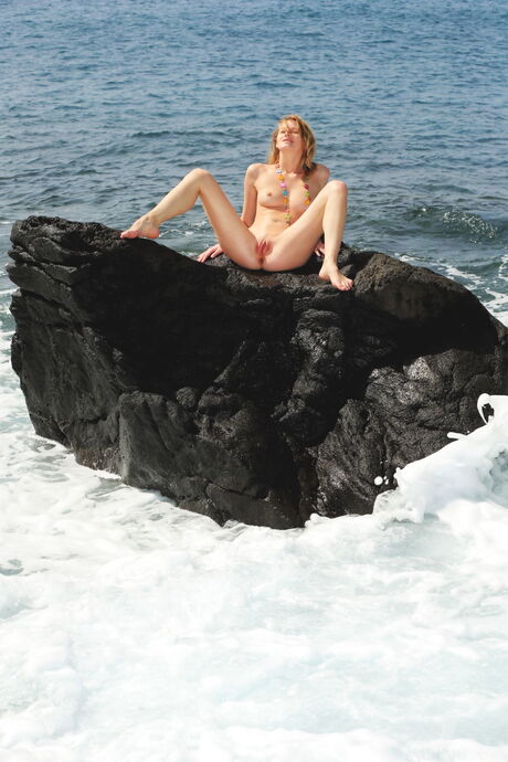 Blond tonåring Mila jag poserar nakna på stenar på stranden medan du bär ett halsband
