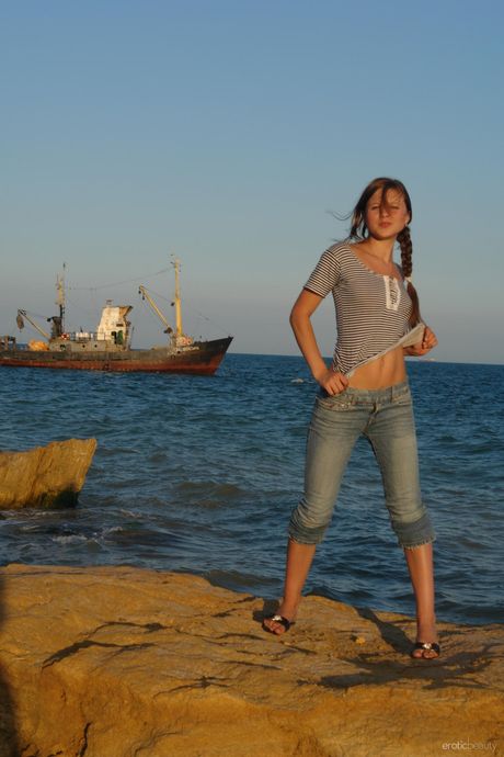 Slender teen Petra E gets naked in sandals on a sandy beach