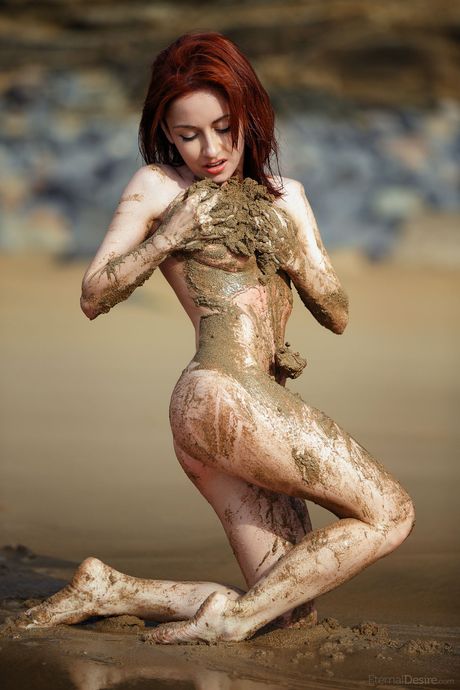 Chuda ruda noc pozuje nago na zacisznej plaży bez nikogo w pobliżu
