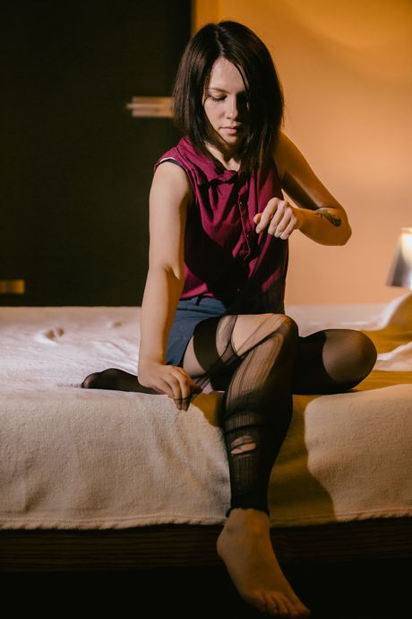 Leuke tiener Alla B verwijdert een zwarte jurk en panty om naakt op een bed te worden
