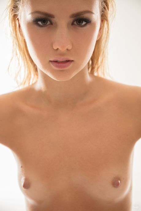 Skinny blonde teen Jati reveals her naked form in heels on a bed in a tempting way