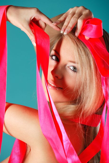 Blonde teen Barbara D removes a bow from her hair while posing in the nude