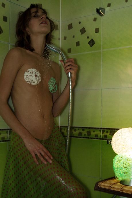 Tigra washes her naked body while standing in a bathtub