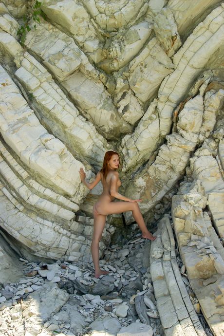 Young redhead Nora F poses totally naked on a sandy beach