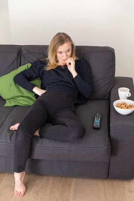 Blond tonåring Aislin tar bort en svart behå och trosuppsättning för att posera naken på en soffa
