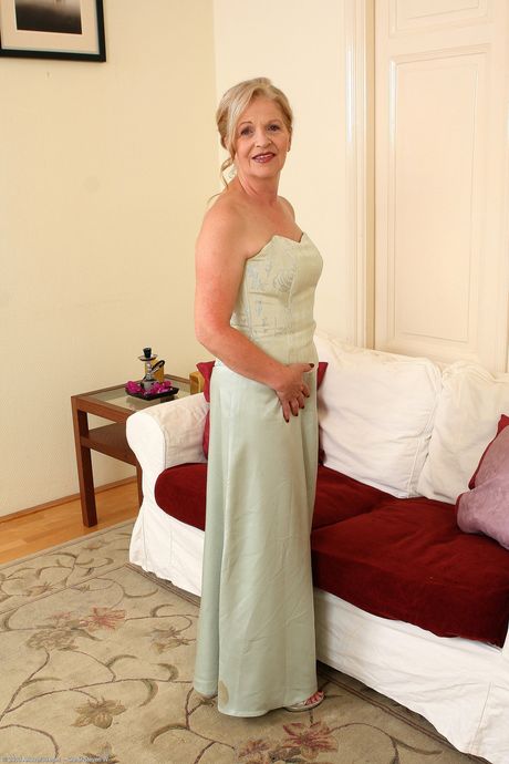 Older woman Nelli removes a dress and lingerie to pose naked on a couch