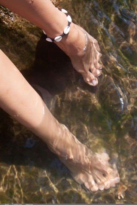 Die junge Brünette Noelia geht nackt an einem felsigen Strand
