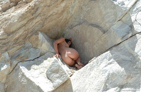 Slim teen Ariana poses naked on a rocky outcrop while masturbating