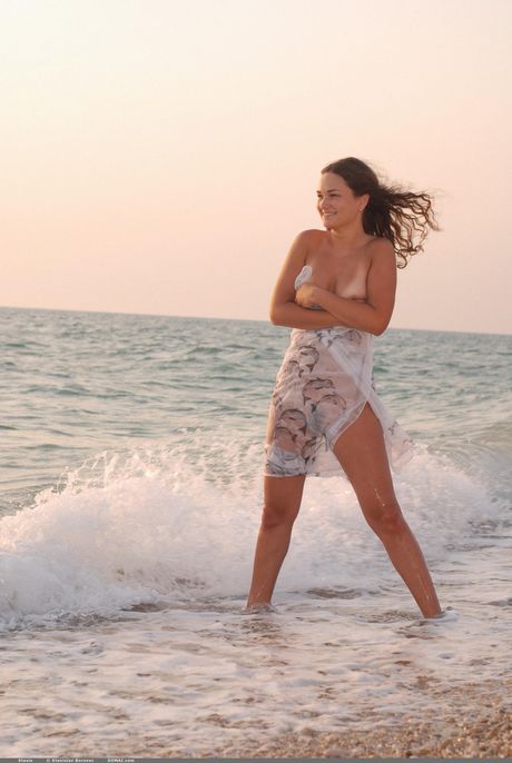 Høj teen stasia poserer nøgen på en sandstrand med sit lange hår flyder
