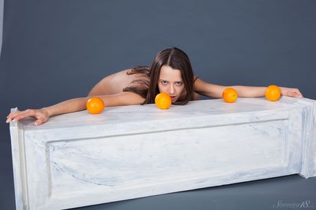 Young brunette Edison X holds a couple of oranges while totally naked