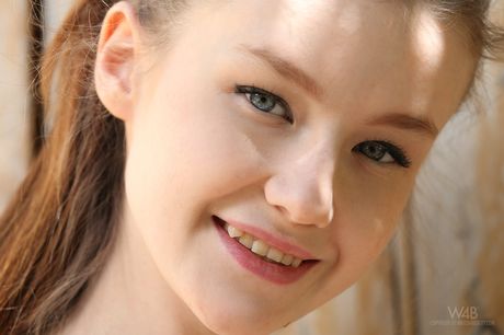 Long haired teen Emily removes a dress to pose nude in a garden