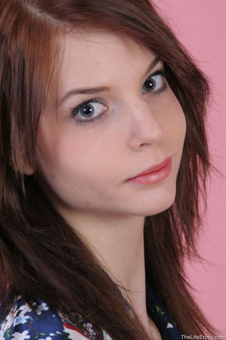 Young redhead Diana E removes her dress and panties to pose nude