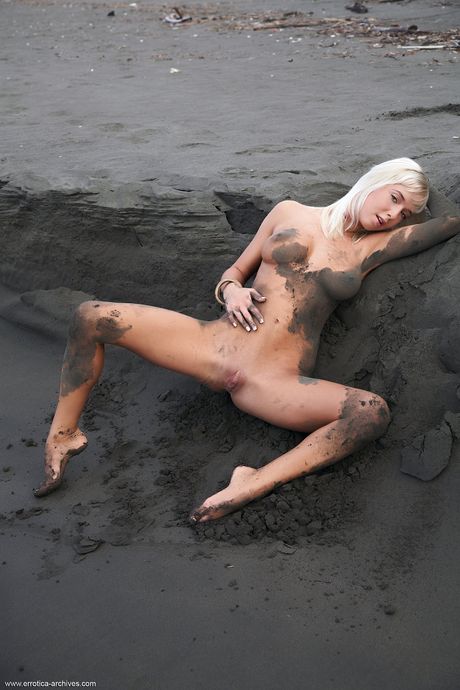 Naked blonde Natali Blond poses on the beach with the ocean in the background